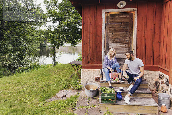 Freunde mit Gemüsekiste sitzen vor dem Haus am See