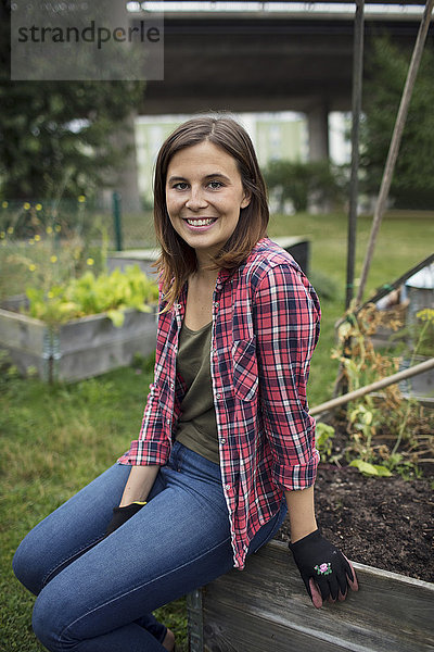 Porträt einer lächelnden erwachsenen Frau  die auf einer Holzkiste im Stadtgarten sitzt.