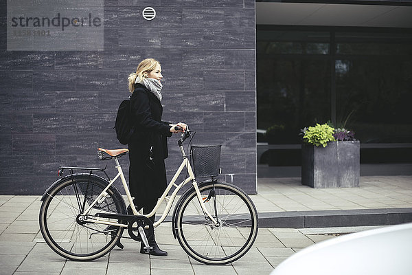 Durchgehende Seitenansicht der mittleren erwachsenen Frau mit Fahrradspaziergang am Gebäude