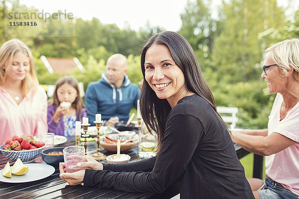 Porträt einer Frau  die mit Freunden und Familie bei einer Gartenparty am Tisch sitzt.