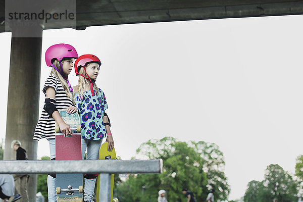 Freunde mit Helmen  die Skateboards halten  während sie im Park gegen den klaren Himmel stehen.