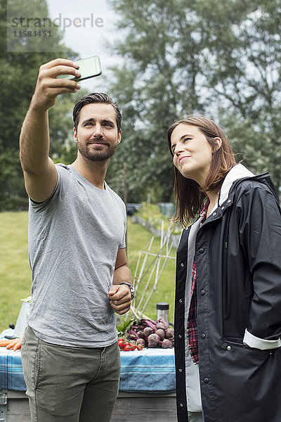 Mittleres erwachsenes Paar nimmt Selfie durch Handy im Stadtgarten mit.