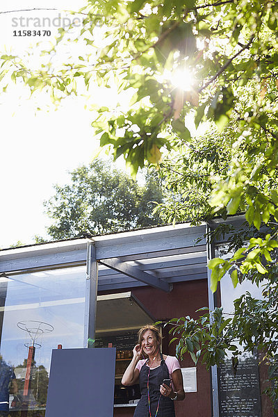 Niederwinkelansicht des Kaffeehausbesitzers über Kopfhörer  die an einem sonnigen Tag mit dem Handy verbunden sind.