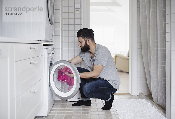 Seitenansicht des Mannes beim Beladen der Wäsche in der Waschmaschine zu Hause