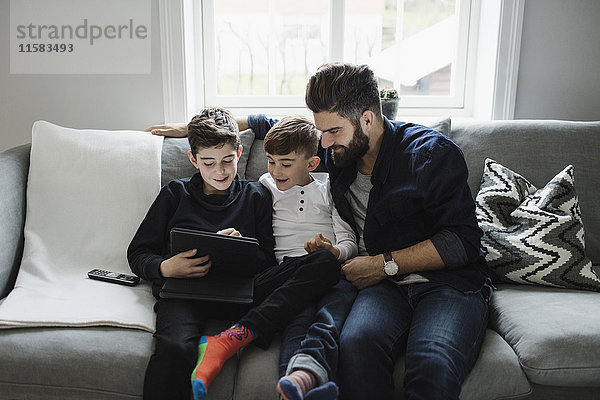Vater und Sohn sehen den Jungen mit dem digitalen Tablett an  während er auf dem Sofa sitzt.