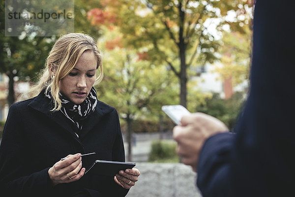 Mittlere erwachsene Geschäftsfrau mit Smartphone und Mann im Vordergrund im Freien