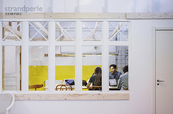 Vier Personen diskutieren in einer Besprechung durch ein Glasfenster im Büro.