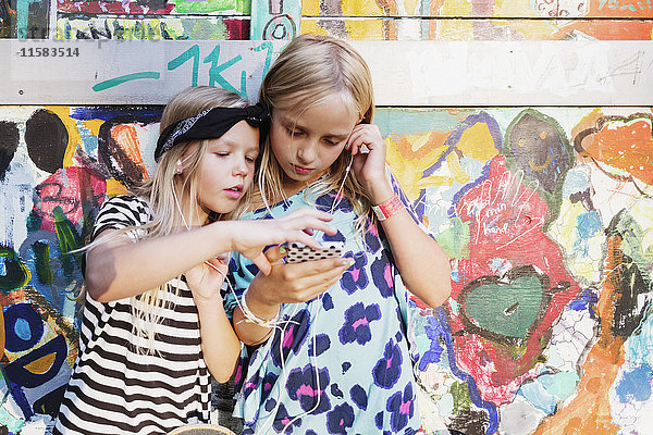 Mädchen  die Musik über das Handy hören  während sie an der Graffiti-Wand stehen.