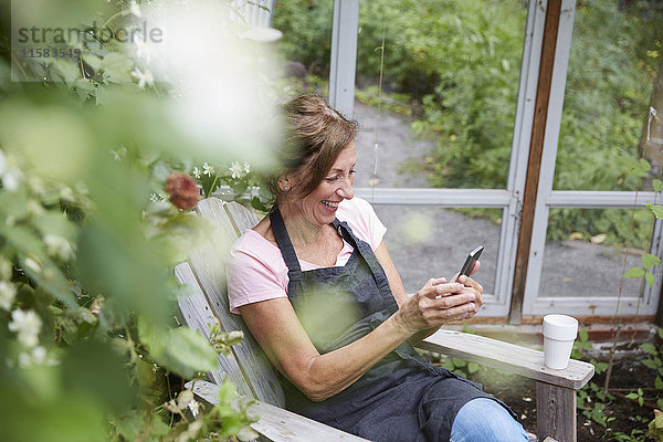 Glückliche Gärtnerin beim Sitzen im Hof mit dem Handy