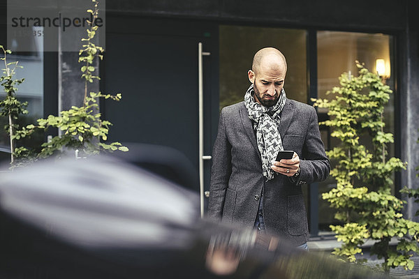 Mid Erwachsenen Geschäftsmann mit Smartphone gegen Gebäude