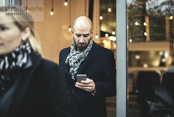 Mittlerer erwachsener Geschäftsmann mit Handy beim Verlassen des Cafés