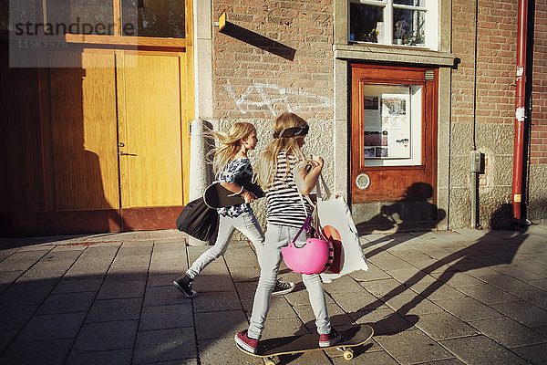 Volle Länge von Freunden mit Skateboards auf dem Bürgersteig bei Sonnenschein