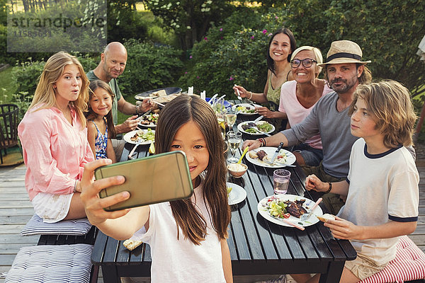 Glückliche Familie und Freunde suchen  während Mädchen  die Selfie vom Handy im Garten während der Gartenparty nehmen.