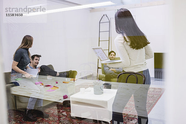 Vier Personen diskutieren im Kreativbüro durch die Glaswand gesehen