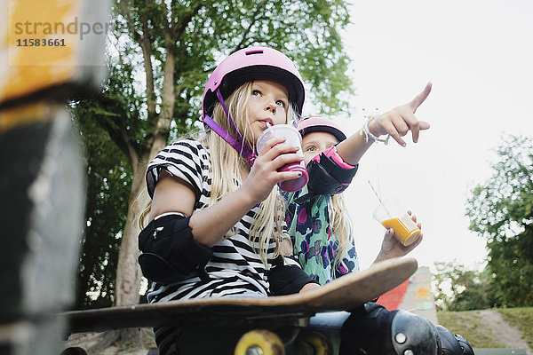 Mädchen  das auf einen Freund zeigt  während es im Skateboardpark Saft trinkt.