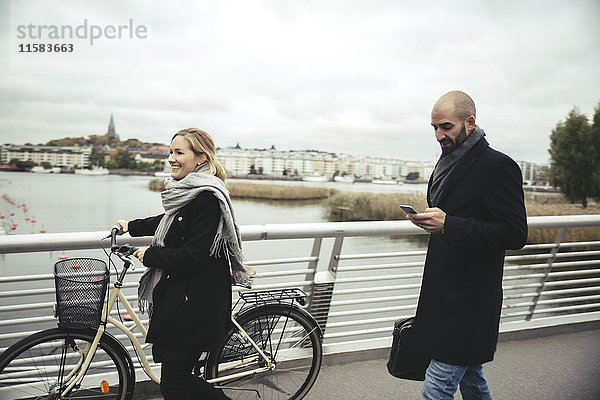 Lächelnde Geschäftsfrau mit Fahrradspaziergang von Geschäftsmann auf Brücke