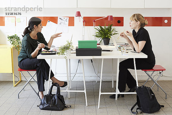 Volle Länge der Geschäftsfrauen beim Mittagessen am Tisch im Büro