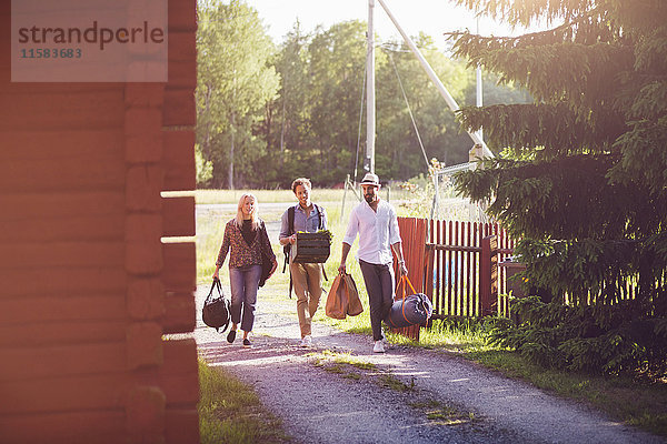 Volle Länge der Freunde  die beim Gehen auf dem Fußweg Gepäck mit sich führen