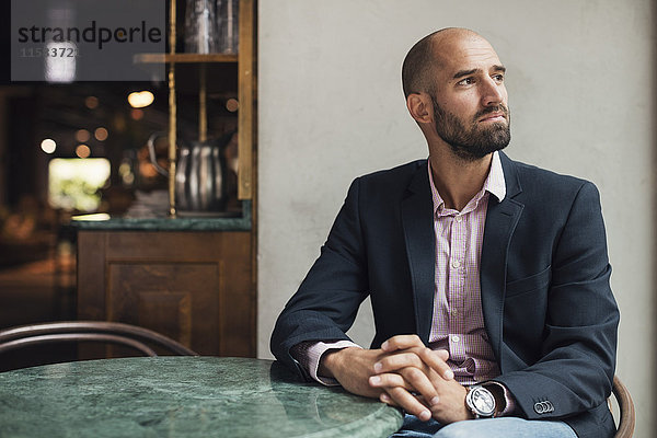 Mittlerer erwachsener Geschäftsmann schaut weg weiß am Tisch im Restaurant sitzend