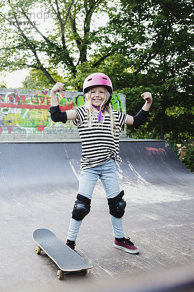 Lächelndes Mädchen  das auf der Skateboard-Rampe steht und seine Muskeln beugt.