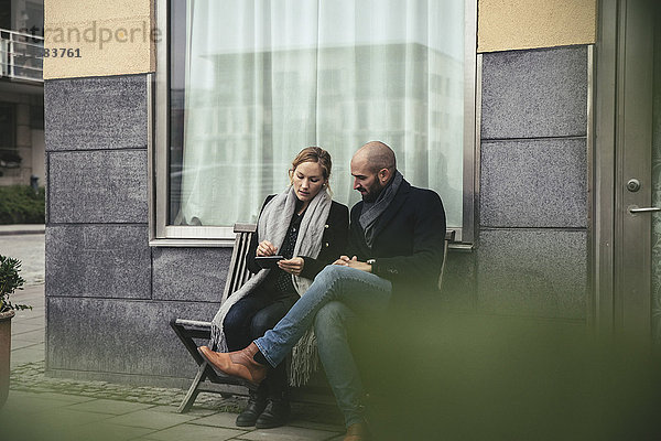 Volle Länge der mittleren erwachsenen Geschäftsleute mit Smartphone auf der Bank gegen Gebäude