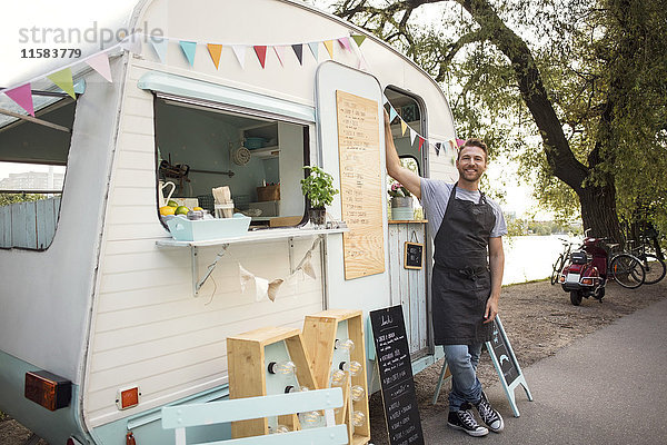 Porträt eines selbstbewussten männlichen Besitzers  der vor einem Food-Truck auf der Straße steht.