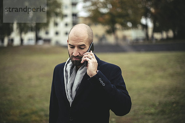 Mittlerer Erwachsener Geschäftsmann  der auf dem Handy im Park spricht.