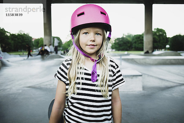 Porträt eines lächelnden Mädchens mit rosa Helm im Skateboardpark