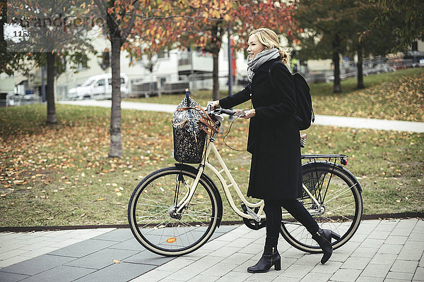 Durchgehende Seitenansicht der Geschäftsfrau mit Radwanderung auf dem Fußweg im Herbst