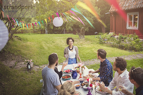 Hochwinkelansicht der Frau  die mit Freunden am Tisch bei der Gartenparty spricht.