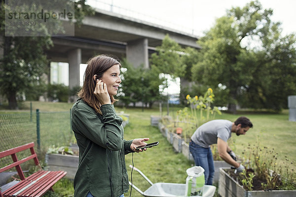 Mittlere erwachsene Frau im Gespräch auf dem Handy mit Mann im Hintergrund im Stadtgarten