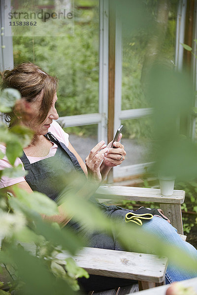 Gärtnerin beim Sitzen im Hof mit dem Handy