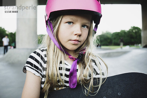 Porträt eines Mädchens mit rosa Helm und Skateboard im Park