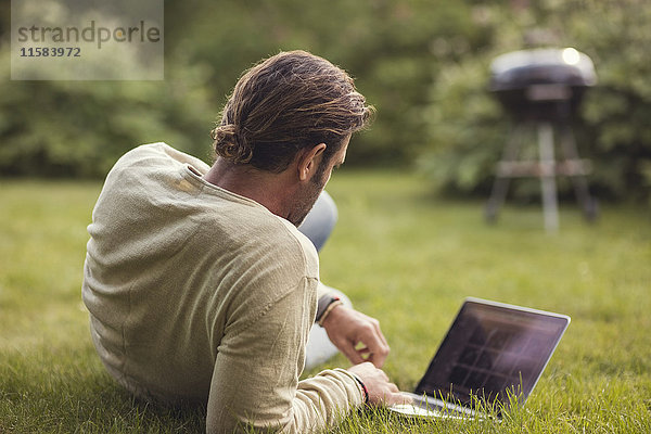 Rückansicht des Mannes mit Laptop auf Gras im Hinterhof