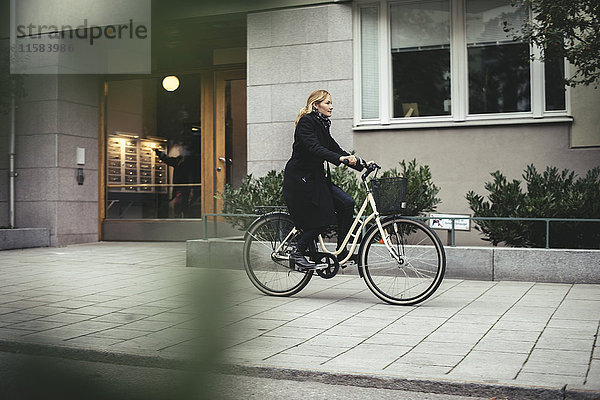 Volle Länge der mittleren erwachsenen Geschäftsfrau auf dem Fahrrad durch die Stadtgebäude