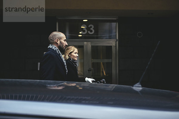 Seitenansicht eines Geschäftsmannes und einer Geschäftsfrau  die am Gebäude vorbeigehen.