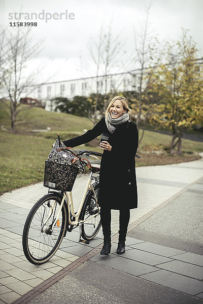 Volle Länge der fröhlichen mittleren erwachsenen Frau mit Fahrrad auf Fußweg