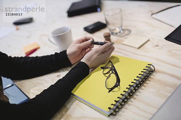 Abgeschnittenes Bild einer jungen Frau  die einen Stift am Schreibtisch im Büro hält.