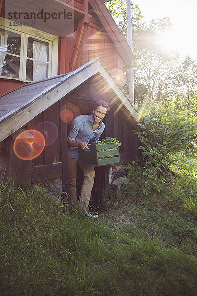 Lächelnder Mann mit Kiste beim Verlassen der Hütte an einem sonnigen Tag