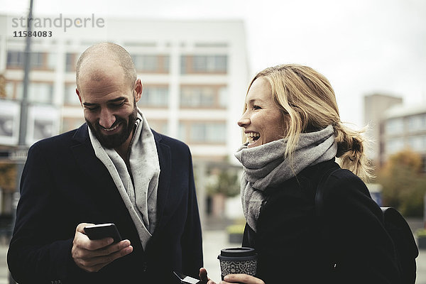 Lächelnde Geschäftsleute mit Smartphones auf dem Bürgersteig in der Stadt