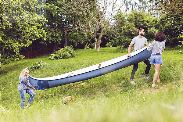 Freunde  die das Kanu auf einer Wiese bei Bäumen tragen.