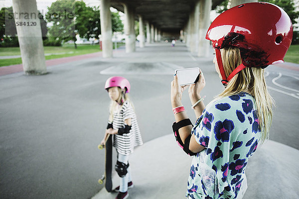 Mädchen fotografiert Freund durch Smartphone im Skateboard-Park