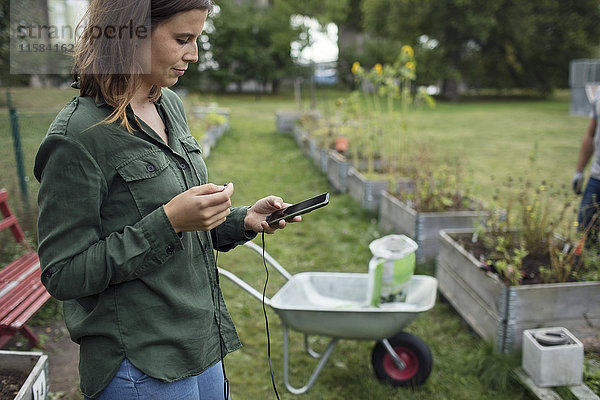 Mittlere erwachsene Frau mit Handy im Gemeinschaftsgarten