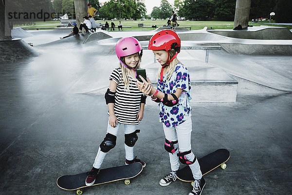 Mädchen zeigt Handy dem Freund im Skateboardpark
