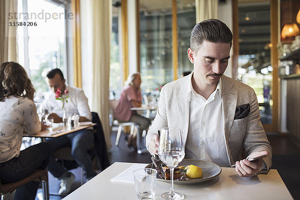 Geschäftsmann beim Mittagessen mit Smartphone im Restaurant