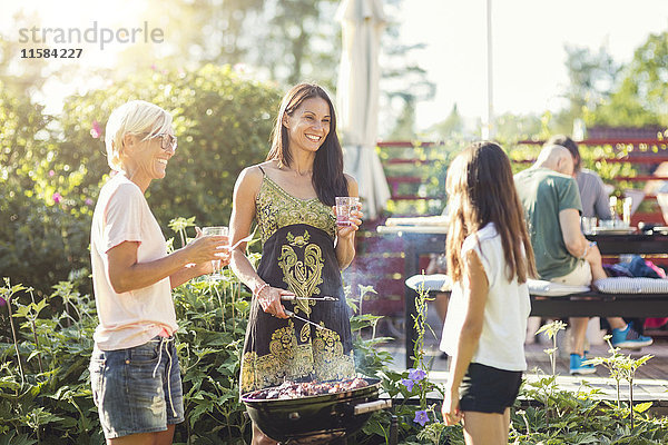 Glückliche Frauen bereiten das Essen auf dem Grill zu  während sie das Mädchen im Garten anschauen.
