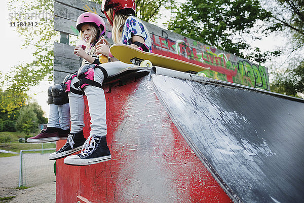 Niedriger Blickwinkel auf Freunde  die Saft trinken  während sie auf der Kante der Skateboard-Rampe sitzen.