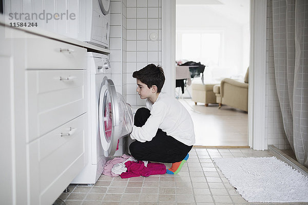 Seitenansicht des Jungen  der die Waschmaschine lädt  während er zu Hause hockt.