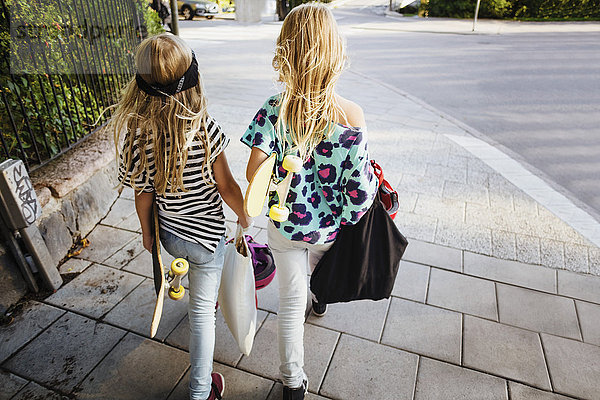 Hochwinkelansicht von Freunden  die Skateboards tragen  während sie auf dem Bürgersteig laufen.