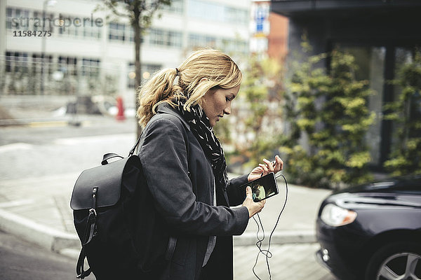 Seitenansicht der mittleren erwachsenen Geschäftsfrau  die ein Smartphone hält  während sie auf der Stadtstraße spazieren geht.